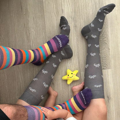 Knee-High Compression Socks in Gray Bicycles and Rainbow Pink – worn by family members at home on a wood floor, lifestyle photo